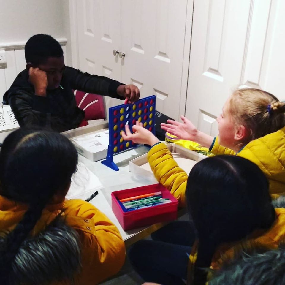 A group of young people sit around a table playing Connect 4