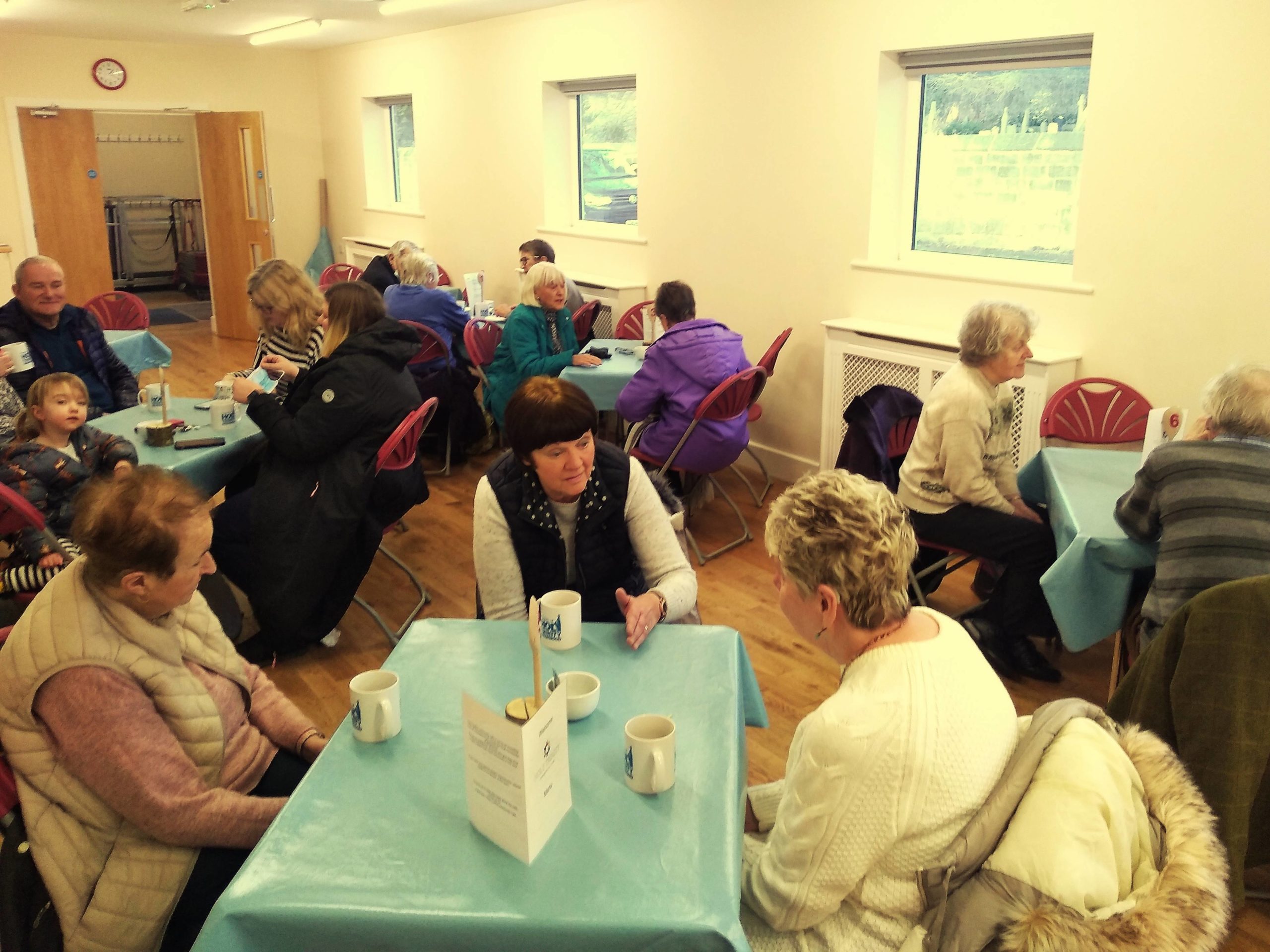 People sat around tables in a community café, talking eating and drinking.